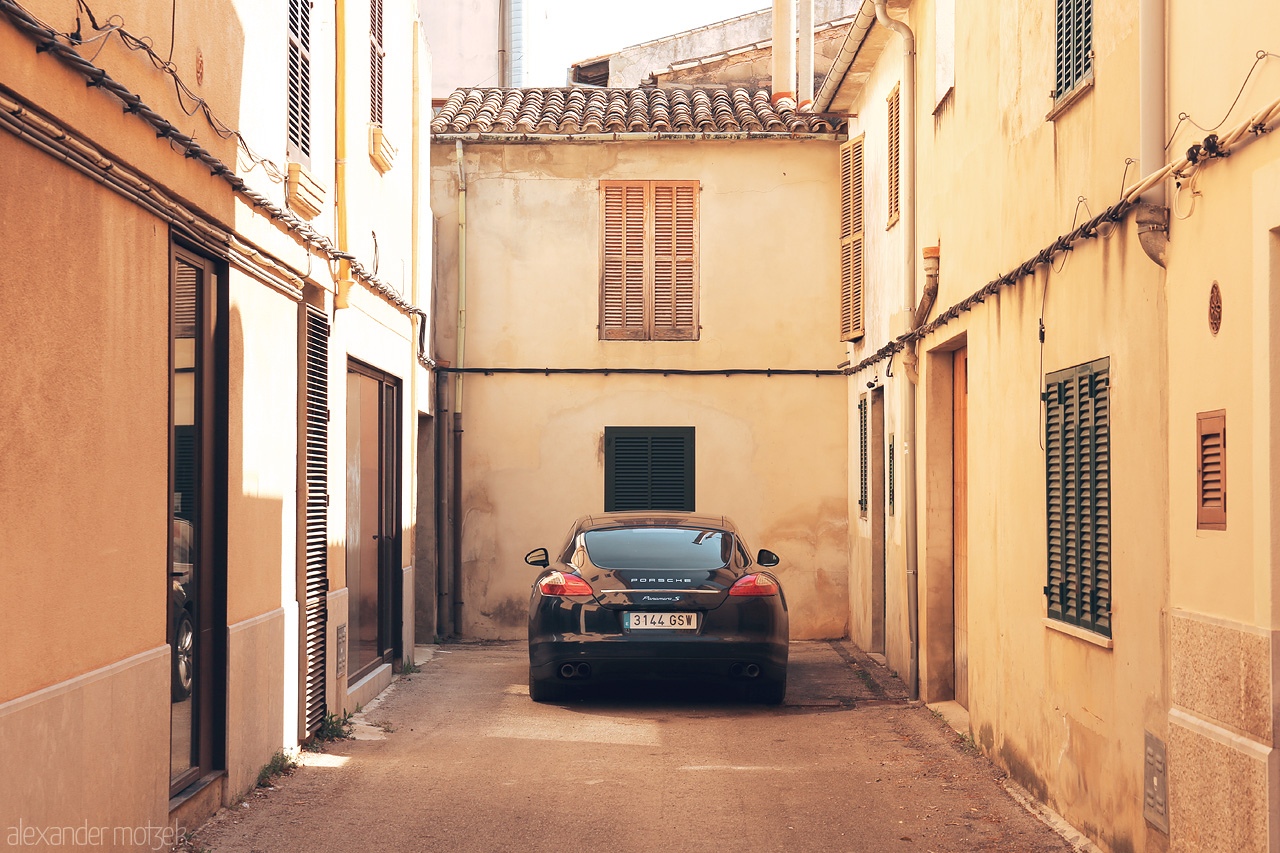 Foto von A sun-soaked alley in Pollença, Mallorca, graced by terracotta rooftops and a solitary parked car.