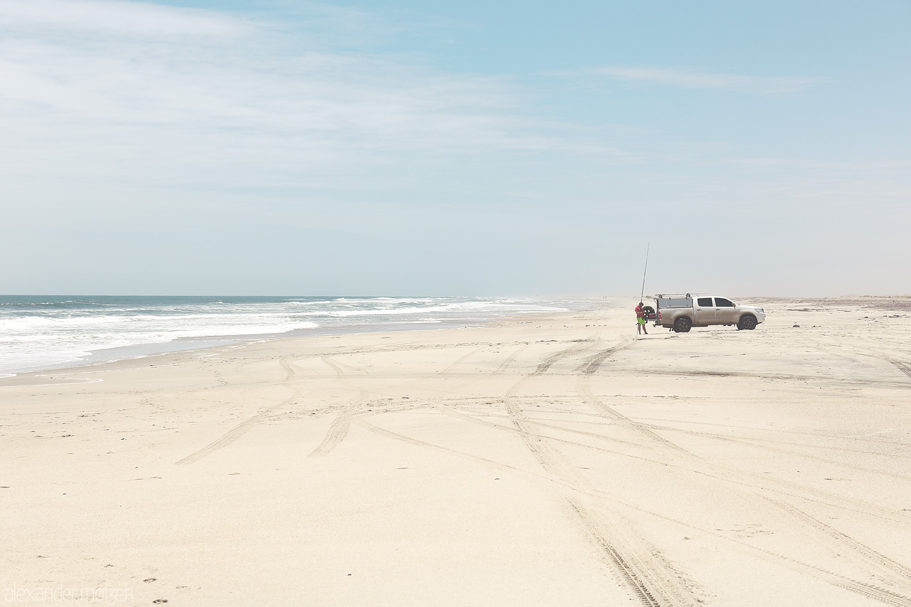 Foto von A lone vehicle and figures against the vastness of Skeleton Coast, Namibia, where desert meets ocean.