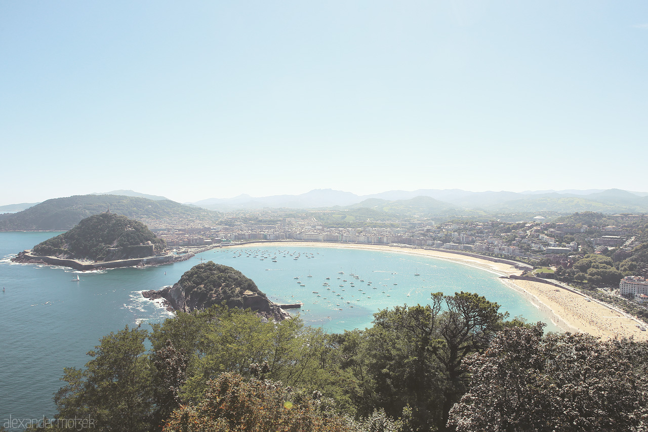 Foto von Panoramic view of San Sebastián's sweeping bay, La Concha Beach, embraced by verdant hills under a clear azure sky.