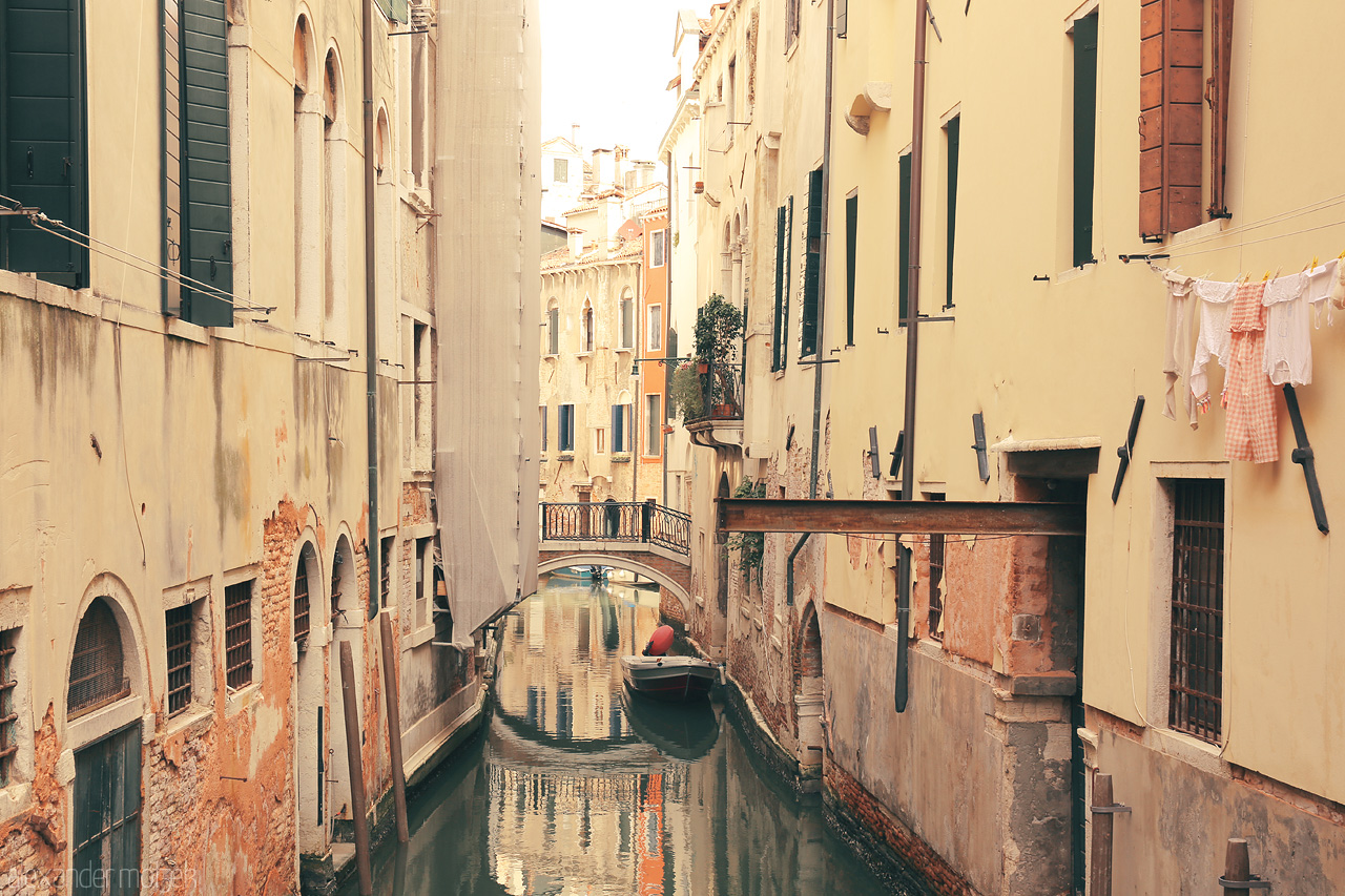 Foto von A calm canal with a gondola, flanked by orange-hued buildings under the soft Venetian sun.