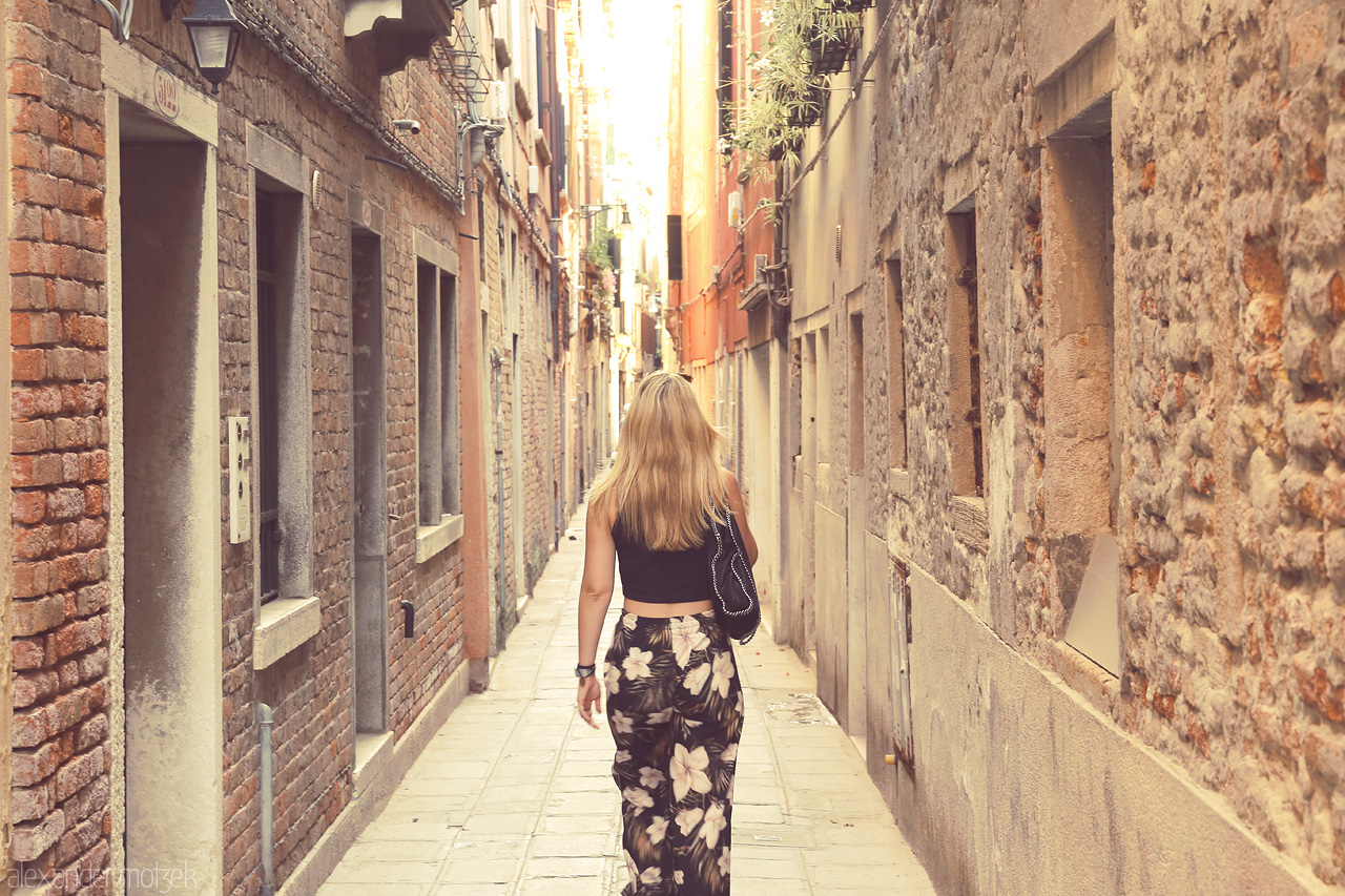 Foto von A lone wanderer strolls down a narrow, sun-kissed alley in the heart of Venice.