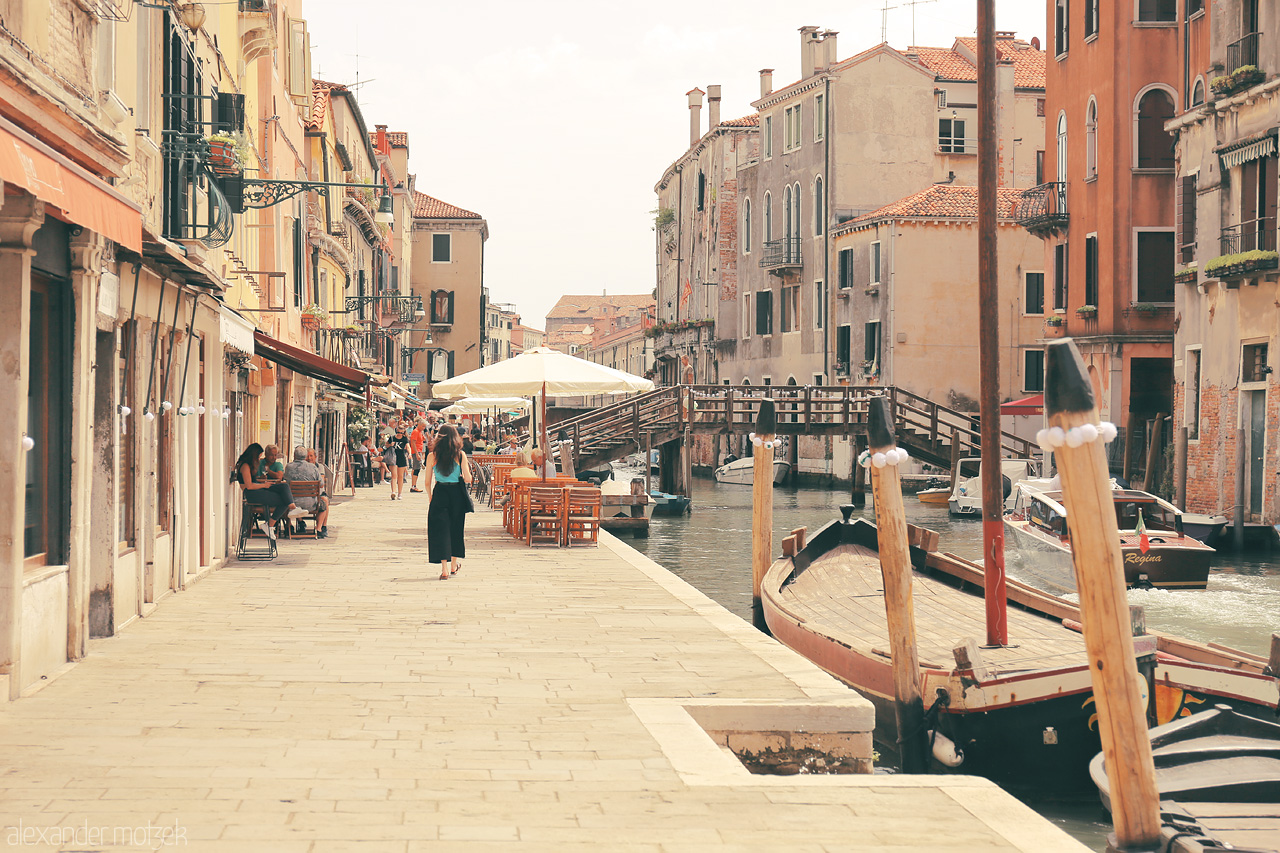 Foto von A warm day in Venice, with gondolas docked along a serene canal flanked by historic buildings and lively terraces.