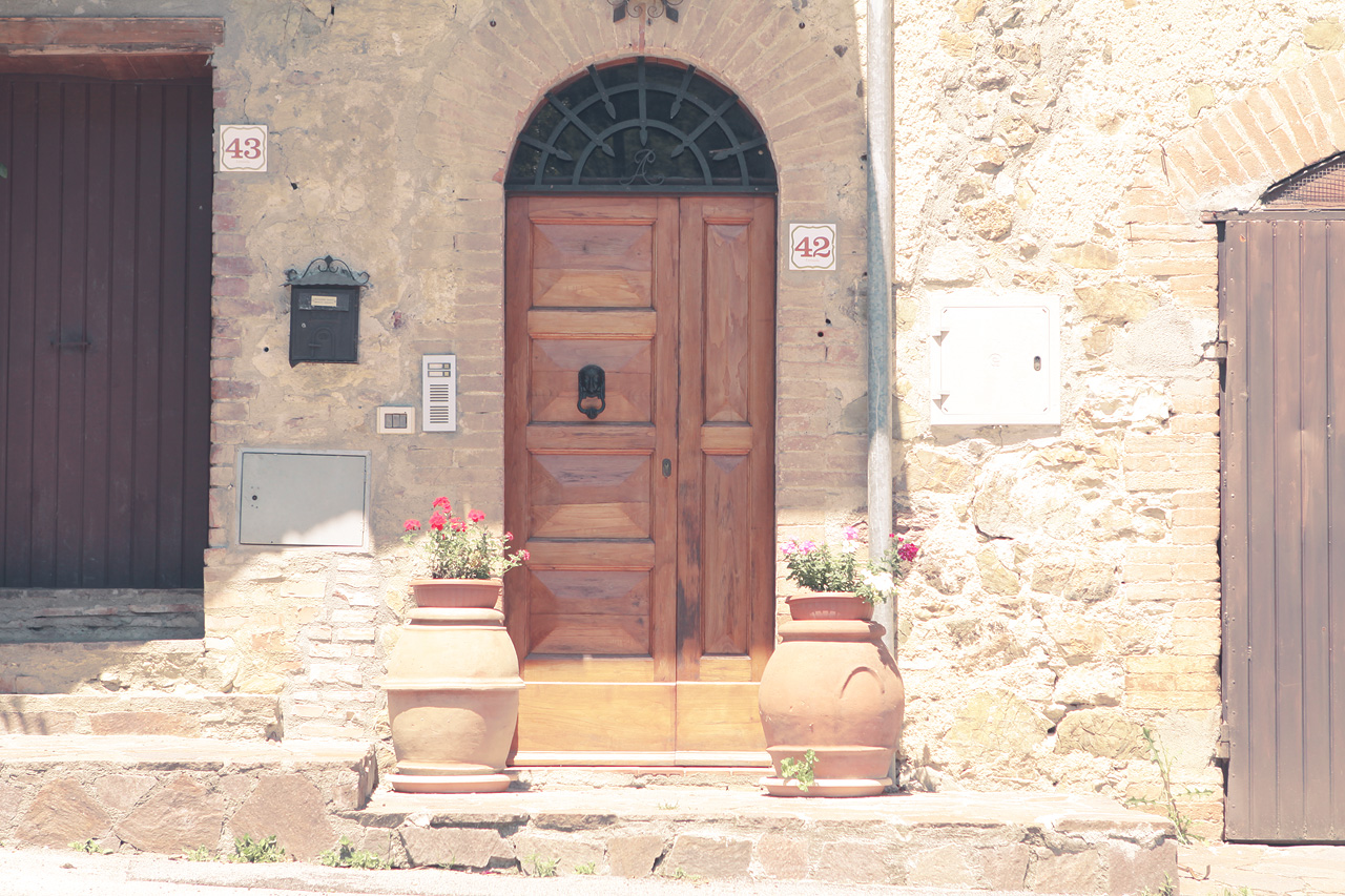Tuscan Doorway Whisper Foto von A charming rustic entrance in Tuscany. Sunlit walls and terracotta pots embody the warm, timeless allure of Italy's countryside.