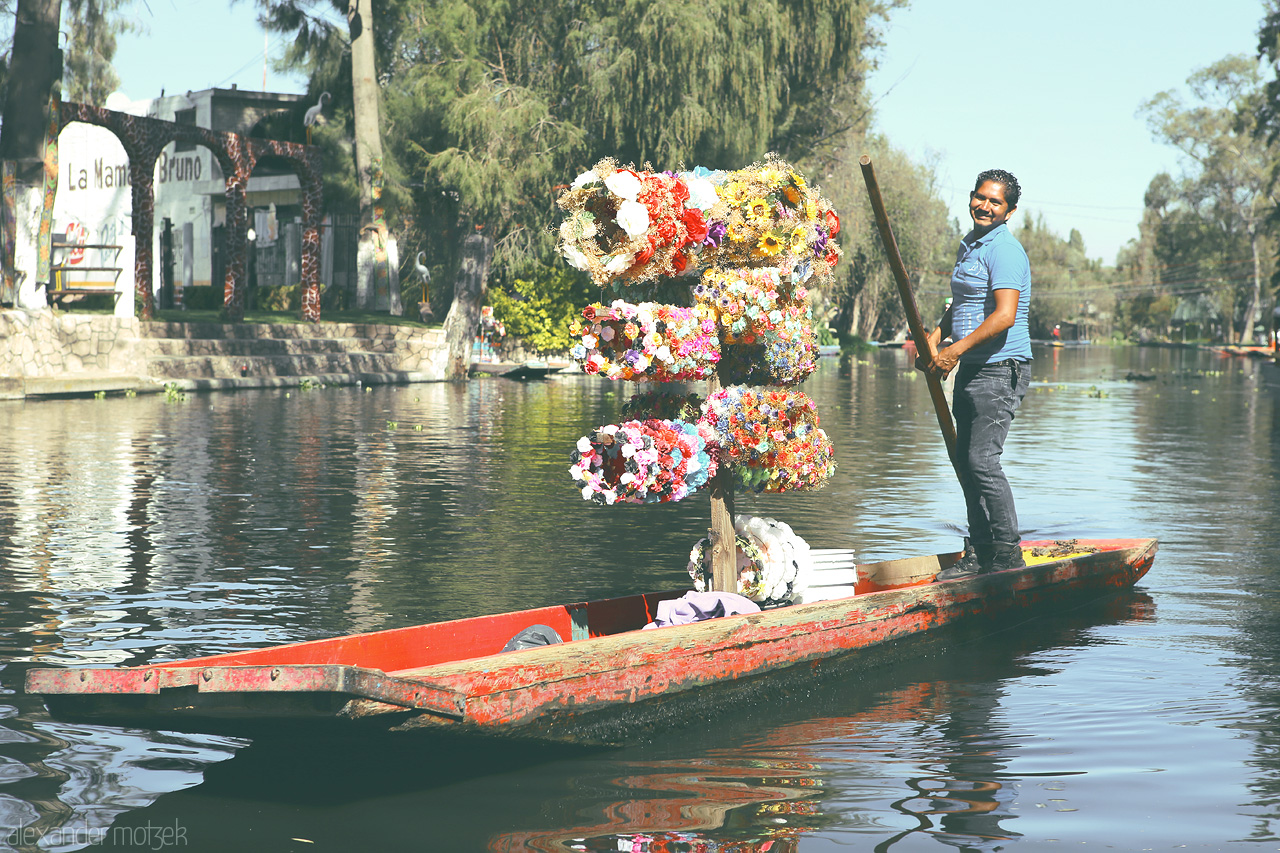 Xochi Flores Foto von A colorful flower boat floats on Xochimilco's canals with a smiling gondolier at the helm.