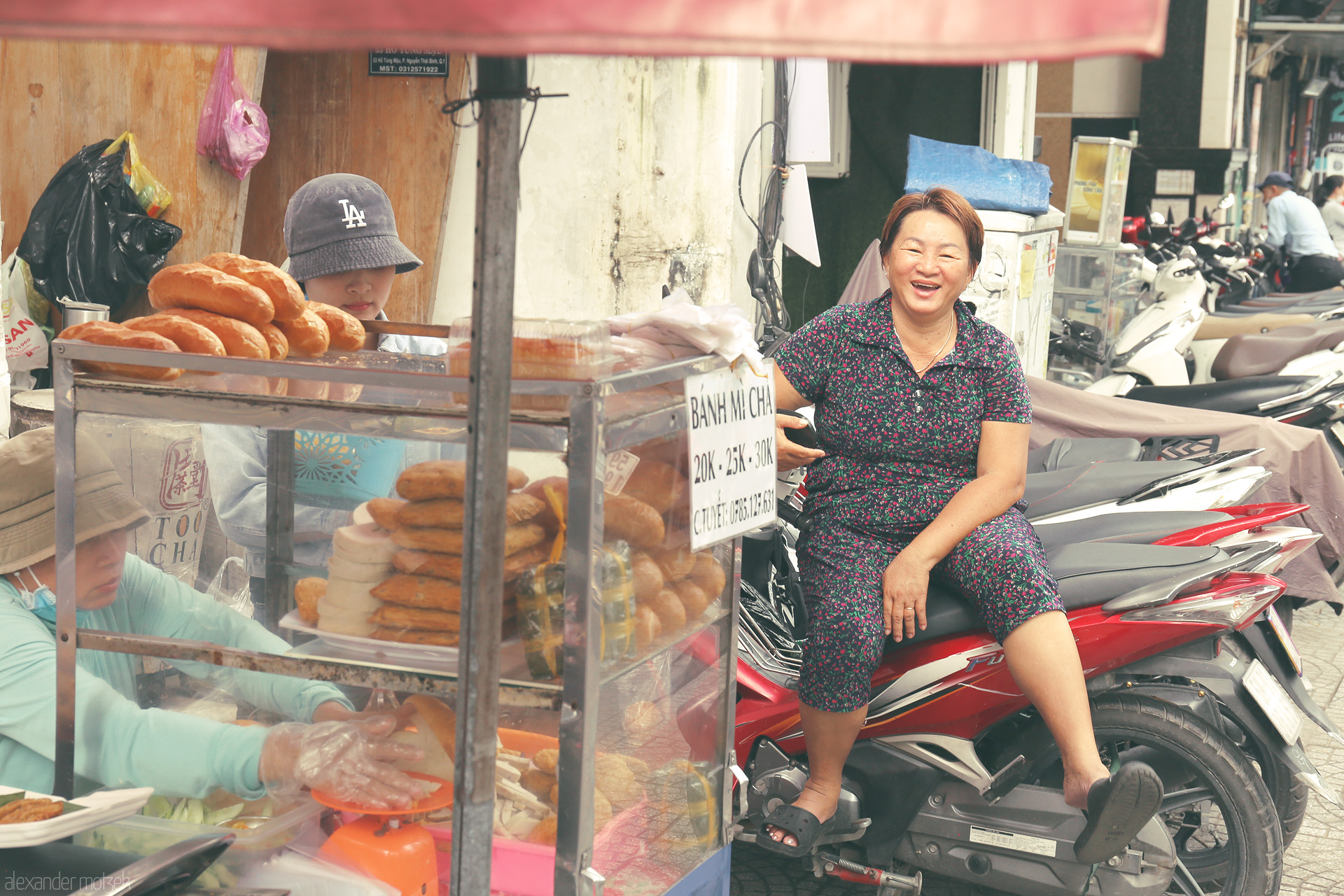Foto von A joyful vendor relaxes beside a bánh mì cart in bustling Ho Chi Minh City, Vietnam, street life alive with flavor and laughter.
