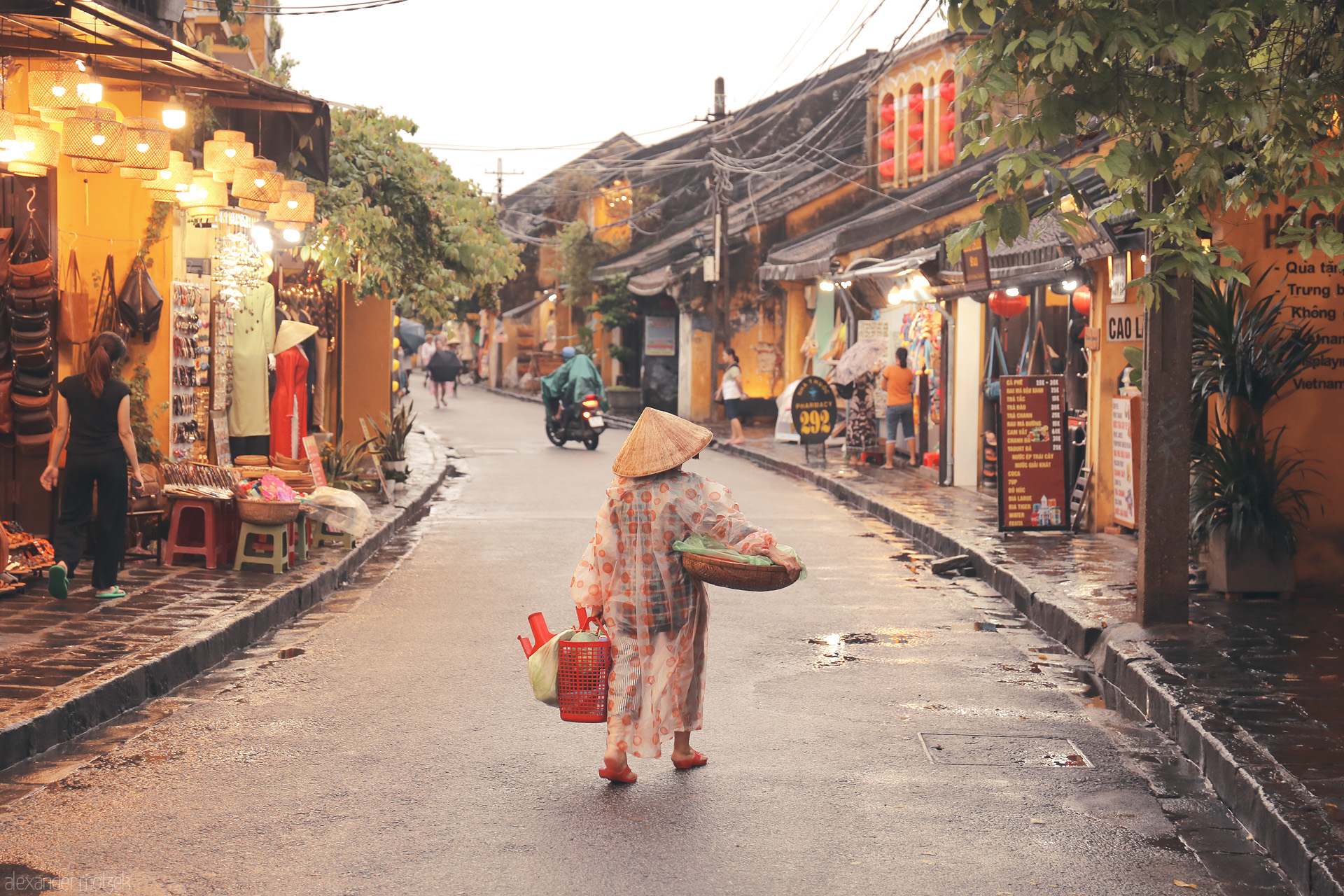 Foto von A lone vendor, bathed in golden light, strolls rainy Hoi An streets under lanterns and conical hats; daily life in Vietnam’s ancient town.