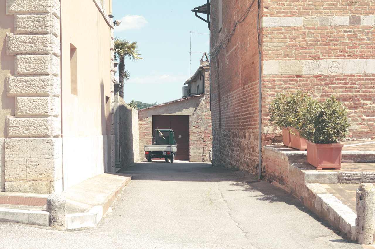 Strada Tranquilla Foto von A quaint alley in Tuscany, Italy, featuring rustic brick walls and a vintage truck under the Italian sun.