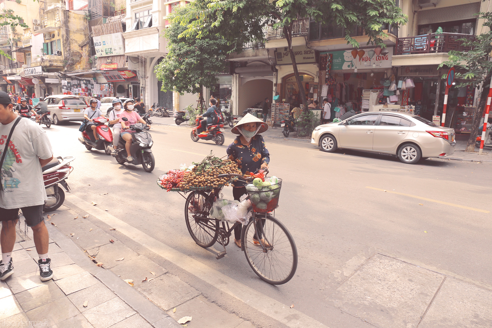 Foto von A street vendor with a fruit-laden bicycle navigates the vibrant Old Quarter in Phuong Hàng Gai, Hanoi.