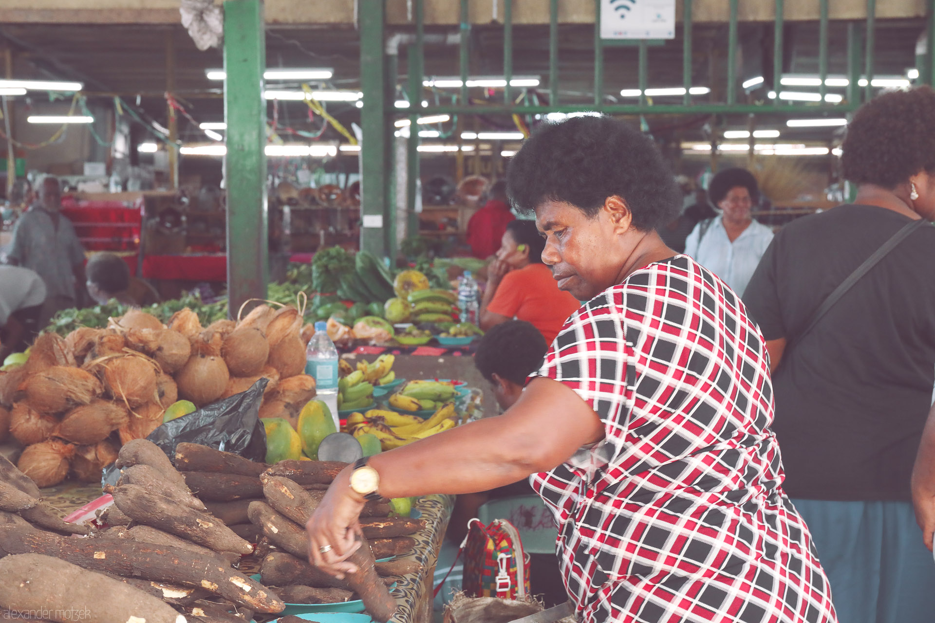 Foto von A vendor sorts cassava and coconuts beside bananas and mangoes at Sigatoka Market, Fiji.