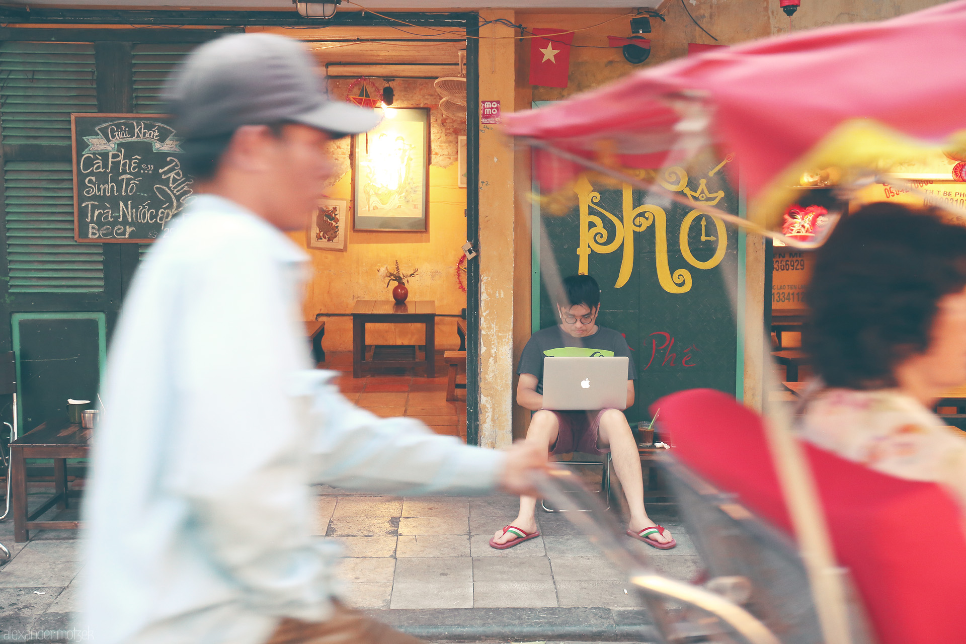 Foto von A young man works on a laptop amid street bustle outside a cozy cafe in Phuong Hàng Bac, Hanoi—modern life in a timeless scene.