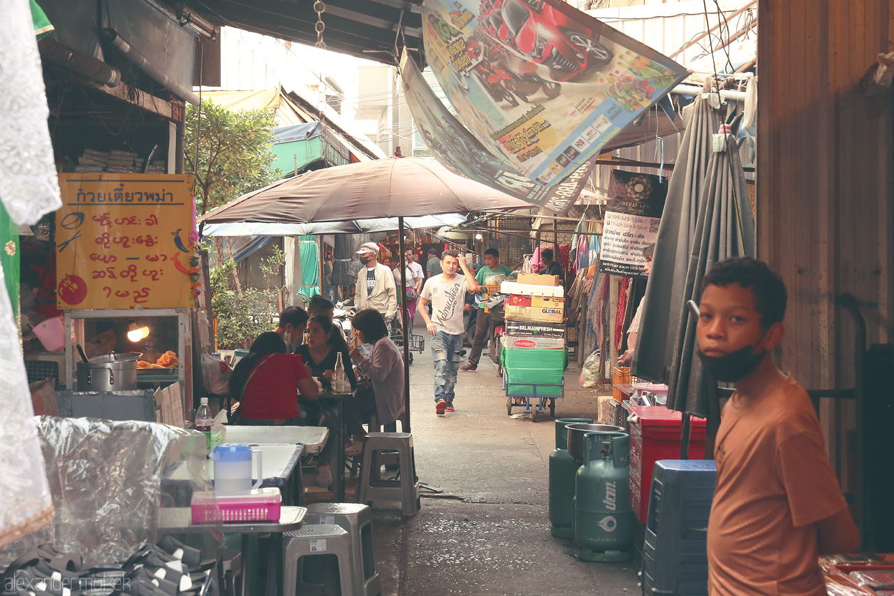 Foto von A bustling alleyway in Wang Burapha, Bangkok captures the vibrant essence of Thai street life with colorful signs and lively locals.