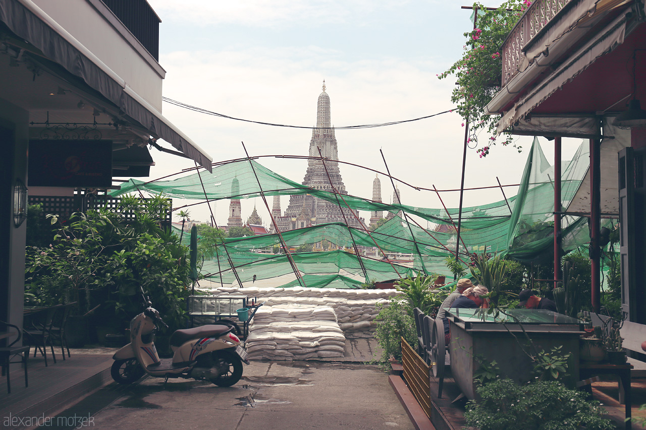 Foto von A street view in Phra Borom Maha Ratchawang, Bangkok, with Wat Arun rising in harmony amid urban life and lush greenery.