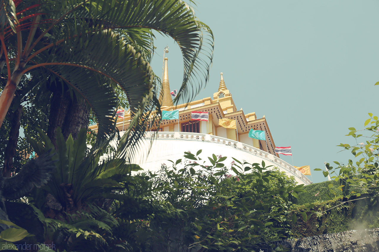 Foto von Glimpse the serene beauty of Wat Saket in Ban Bat, Bangkok, framed by lush greenery against a serene sky.