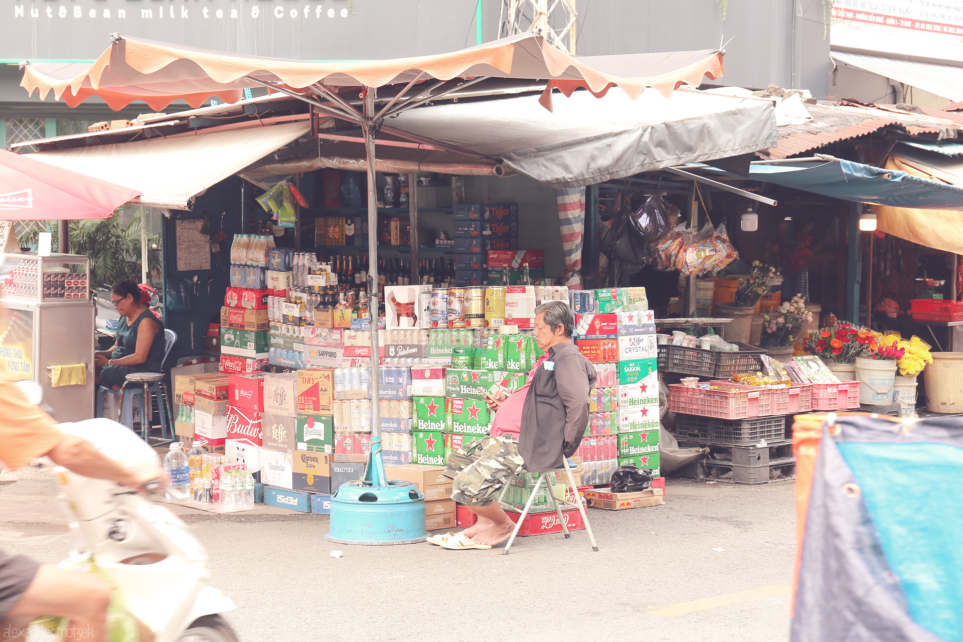 Foto von Breezy street market in Ho Chi Minh City, beer crates stacked, vendors resting, and motorbikes rushing past blooms and daily life.