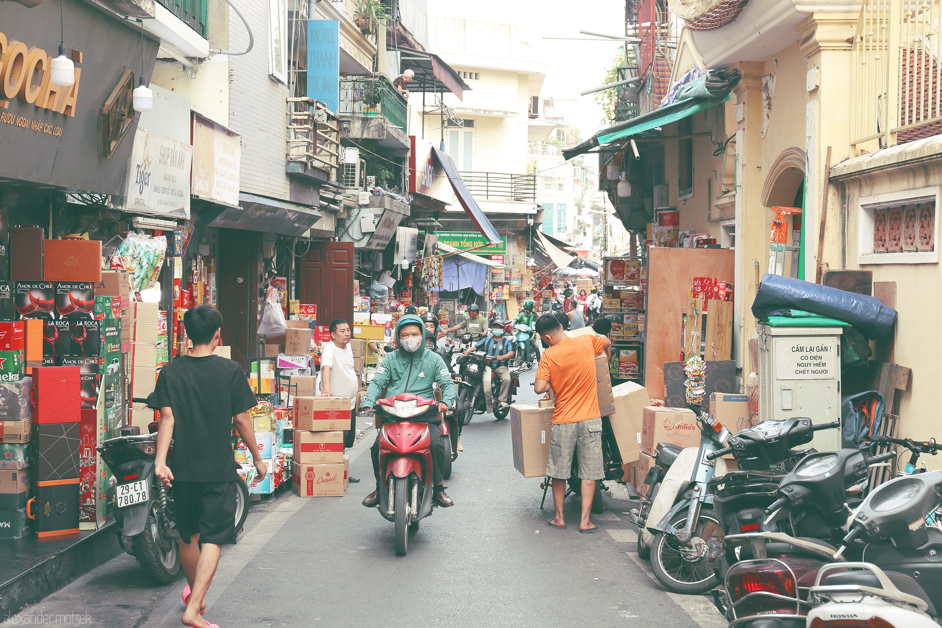 Foto von Bustling alley of Hàng Buồm, Hanoi, alive with scooters, stacked boxes, and vibrant daily street life.