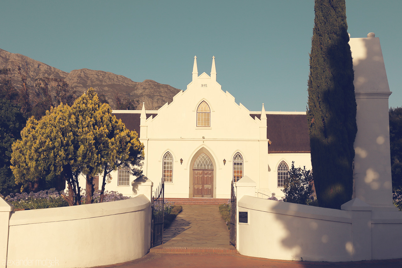 Foto von Classic Cape Dutch architecture shines against the Franschhoek mountains, enveloped by a serene garden in South Africa's wine country.