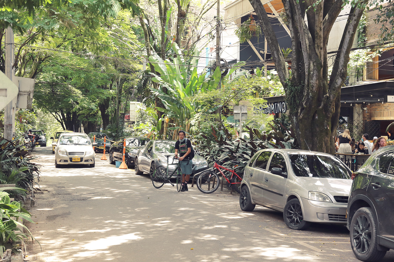 Foto von A bicyclist pauses on a tree-lined street in El Poblado, Medellín, Colombia. Lush greenery surrounds this vibrant, trendy neighborhood.