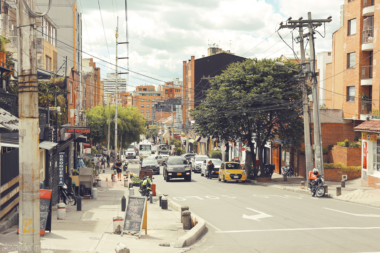 Foto von A bustling street in Chapinero, Bogotá, Colombia, featuring vibrant buildings, busy traffic, and lively city life under a partly cloudy sky.