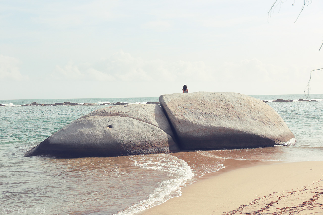 Foto von A person sits atop giant boulders by the shore in Tayrona, Santa Marta, Colombia, embracing the sea and sky's tranquil symphony.