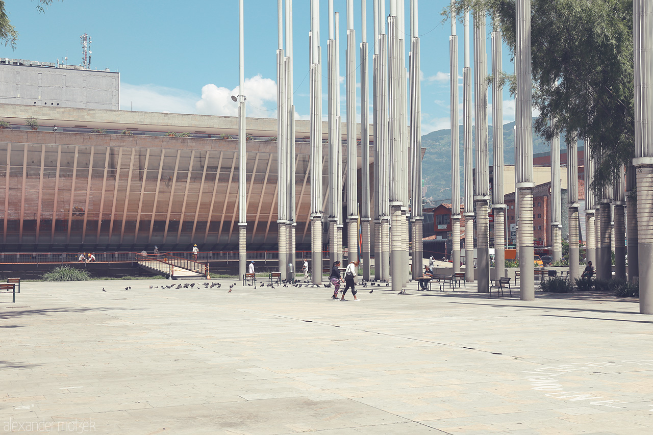 Foto von A serene day in Comuna 10 - La Candelaria, Medellín, where towering pillars shade the plaza, blending the urban landscape with mountain views.