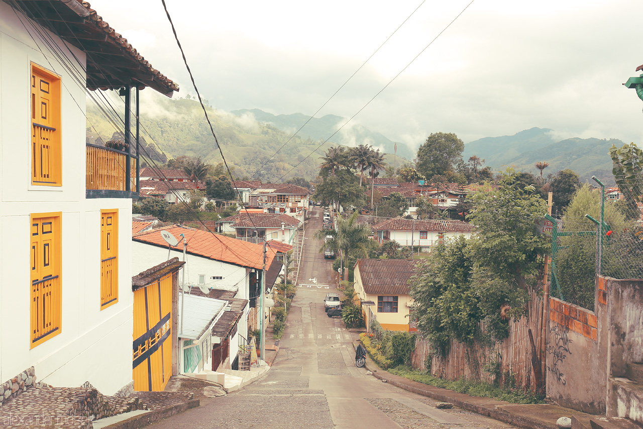 Foto von A tranquil street in Salento, Quindío, Colombia, framed by colorful houses and lush mountains under a cloudy sky.