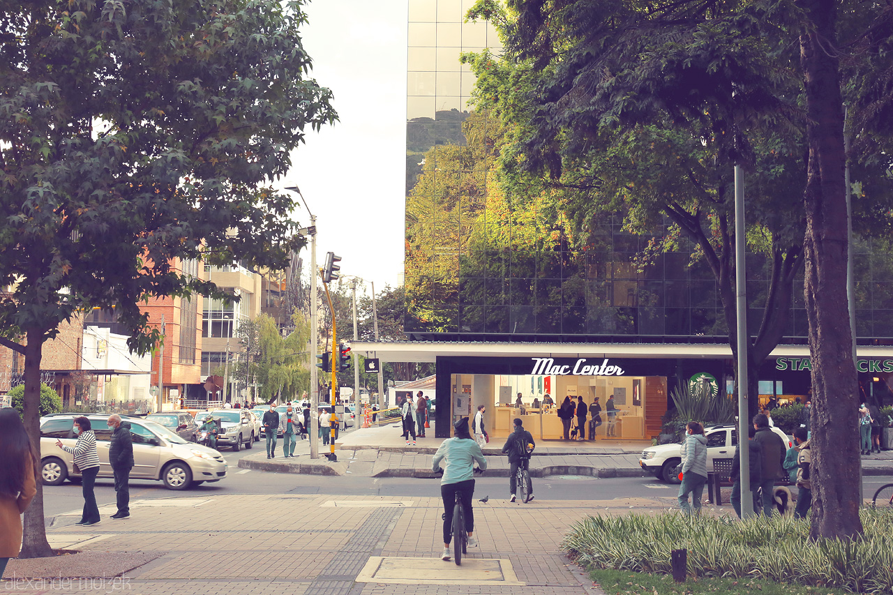 Foto von A tranquil street scene in Chapinero, Bogotá captures a blend of modern life and nature with people strolling, cycling, and reflecting buildings.