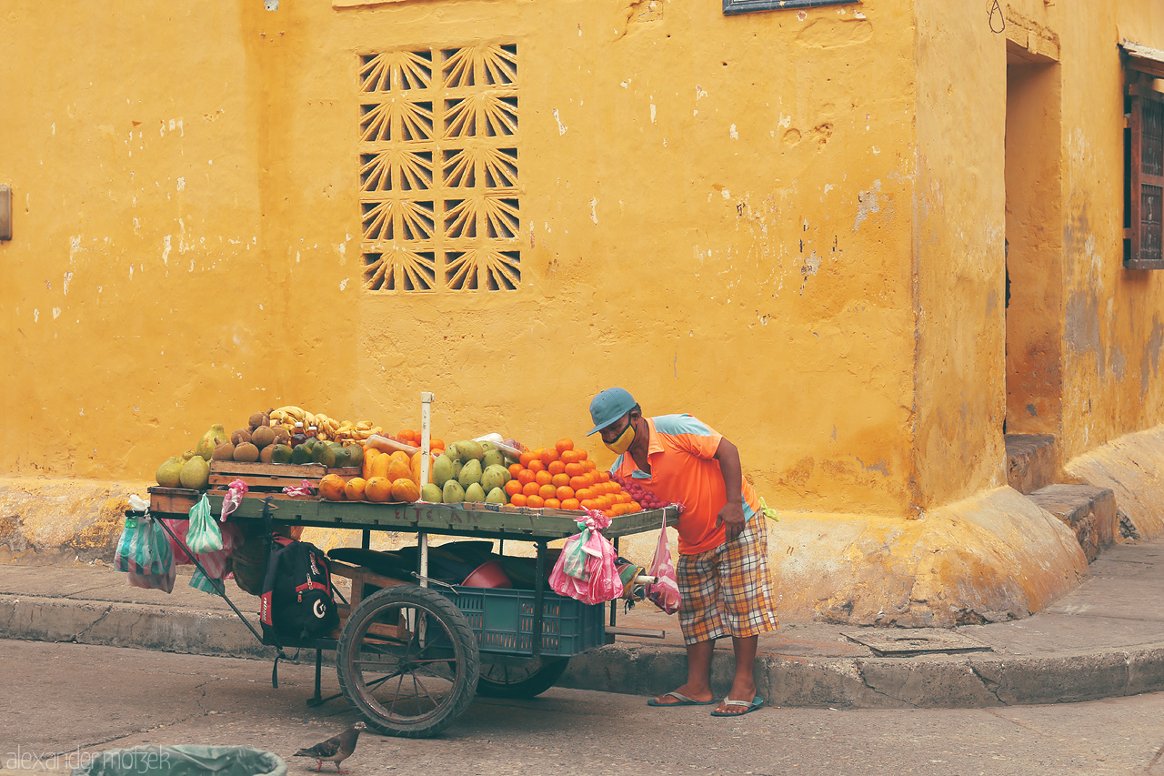 Foto von A vibrant fruit vendor in the colorful streets of Cartagena, Colombia, offering tropical delights under the warm yellow hues of colonial architecture.