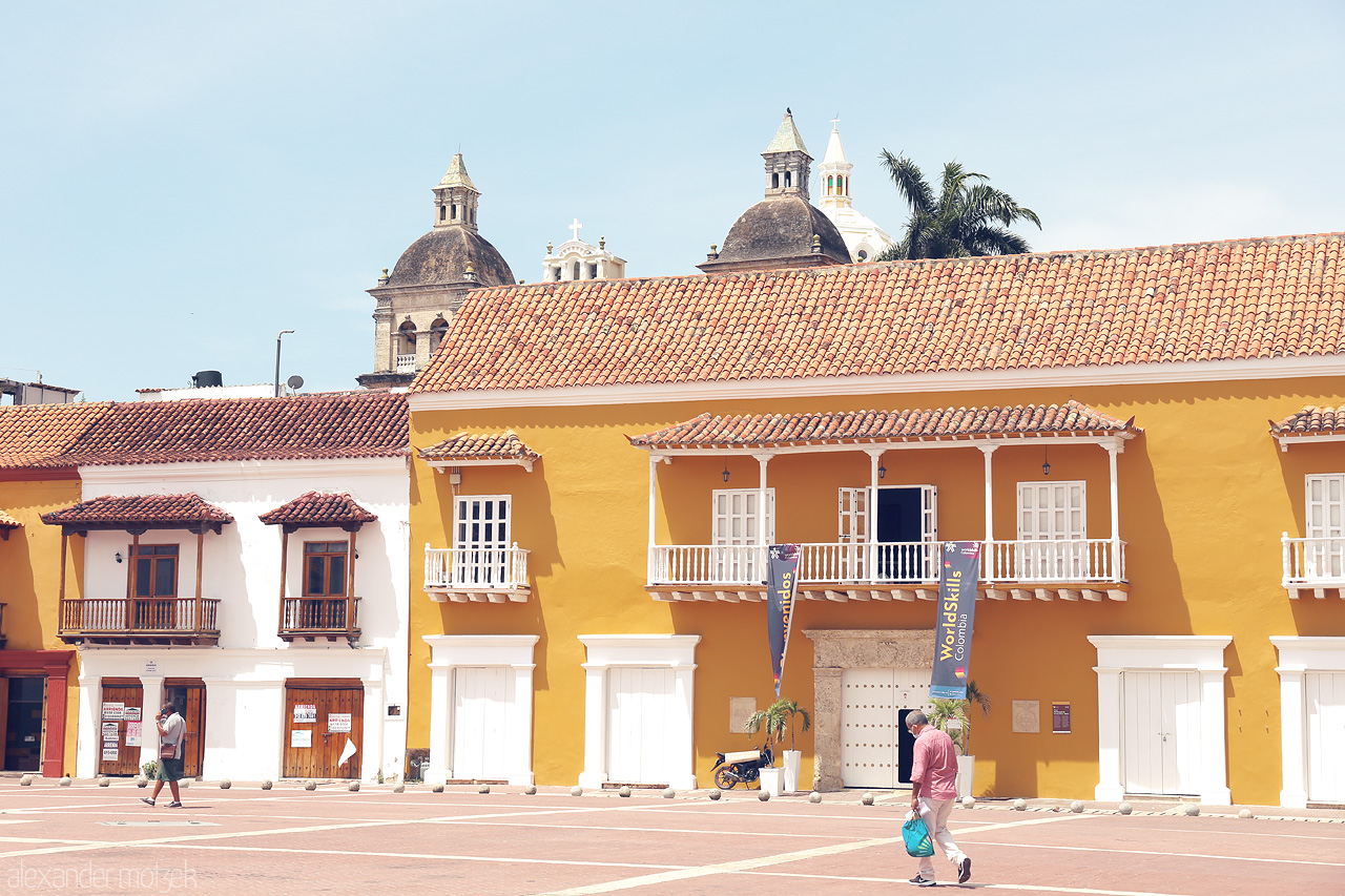 Foto von Bright yellow colonial buildings under a clear sky at Plaza San Pedro Claver in Cartagena, Colombia with church domes in the backdrop.