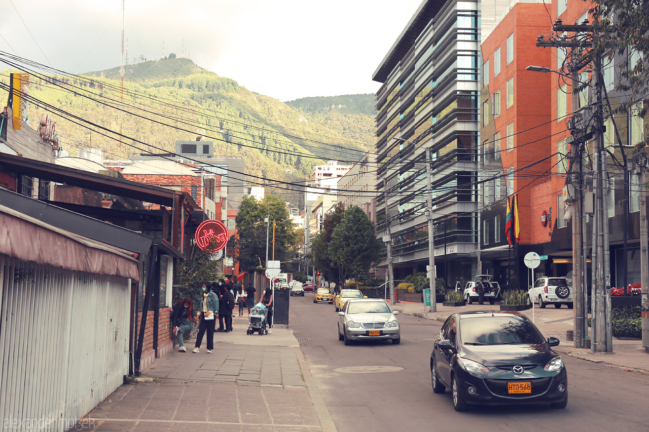 Foto von Chapinero, Bogotá - a lively street with modern buildings, colorful taxi cabs, and breathtaking mountain views in the backdrop.