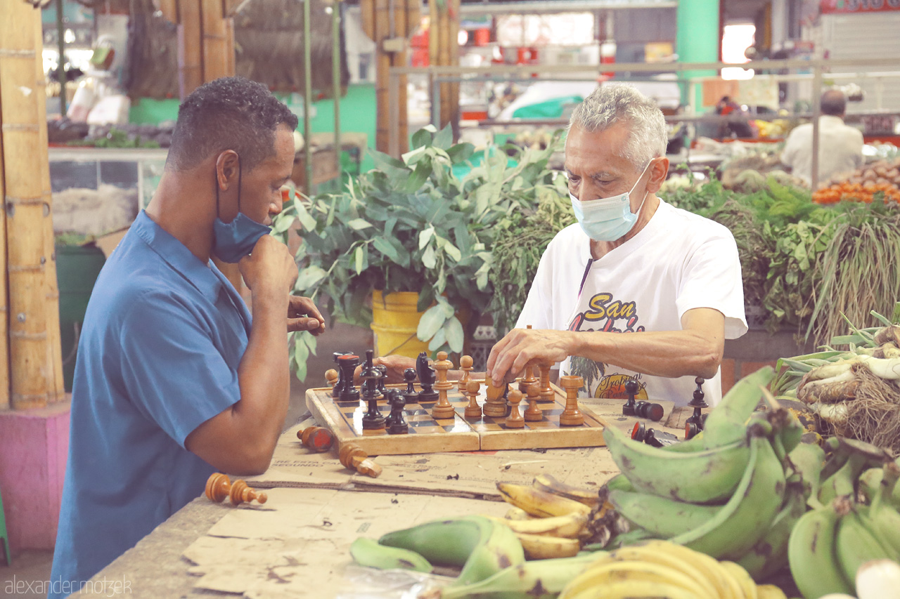 Foto von In Comuna 19, Cali, Colombia, two men engage in a game of chess amidst a lively market filled with fruits and local produce.