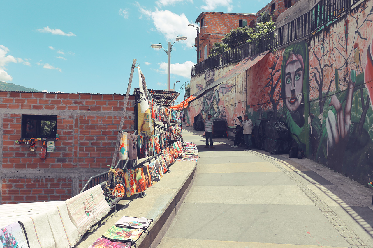 Foto von Street art and colorful market stalls along a sunlit walkway in Comuna 13, Medellín, showcasing the vibrant spirit of the neighborhood.