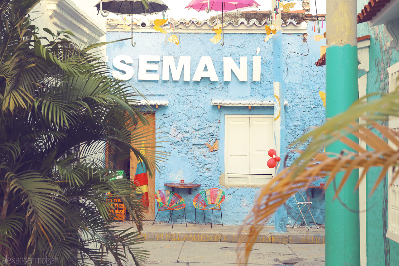 Foto von Vibrant street scene in Cartagena, Colombia with colorful chairs and a blue wall adorned with butterflies and balloons.