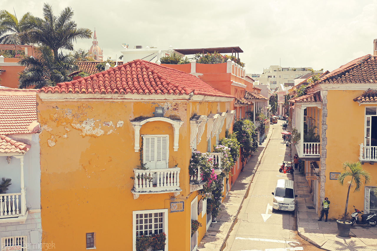 Foto von Vibrant yellow colonial buildings line a charming street in Cartagena, Colombia, with lush greenery and tropical vibes under a hazy sun.