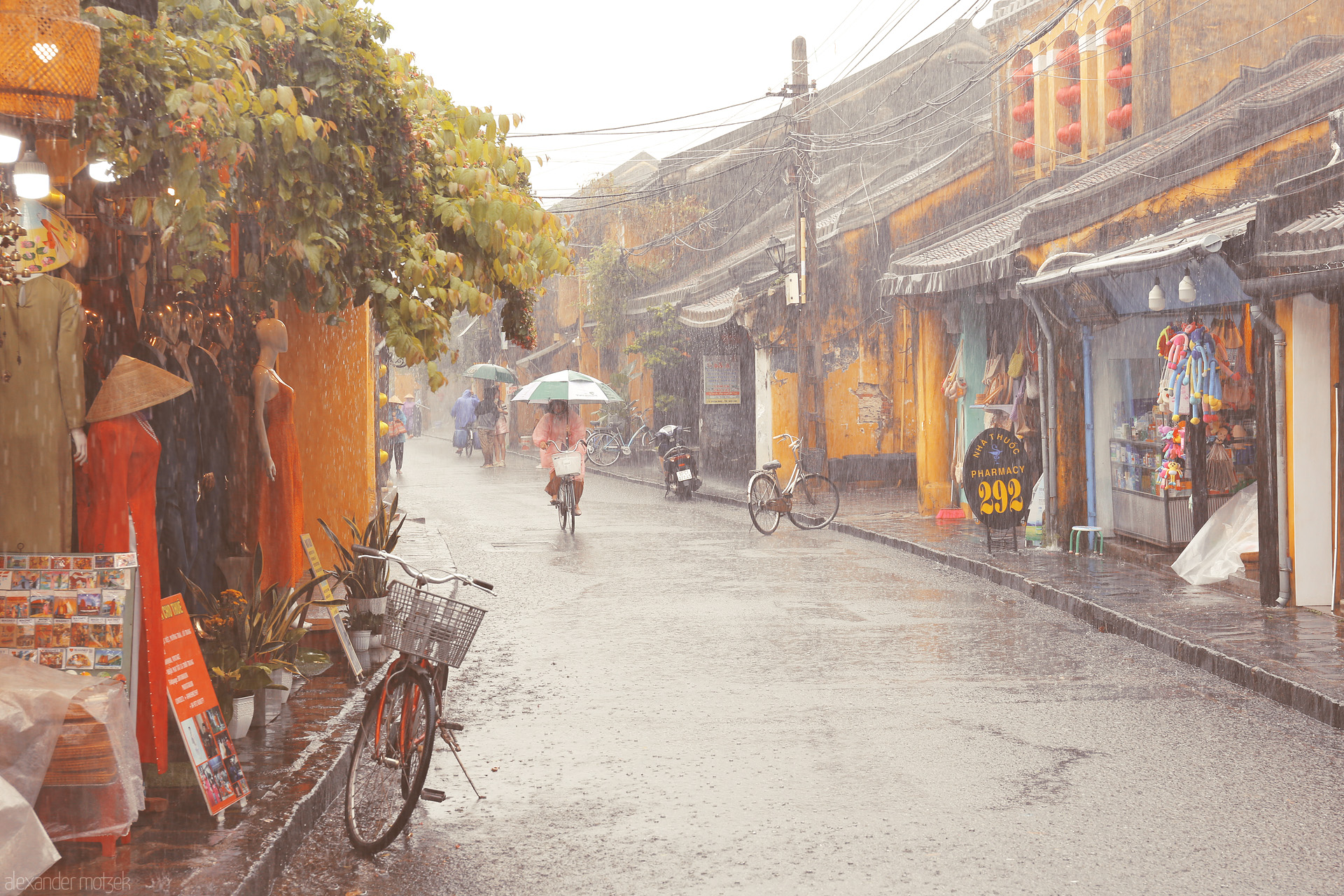 Foto von Cyclists and street life soak in golden rain showers in Hoi An, Vietnam, blending áo dài elegance and vibrant lantern-lit shops.