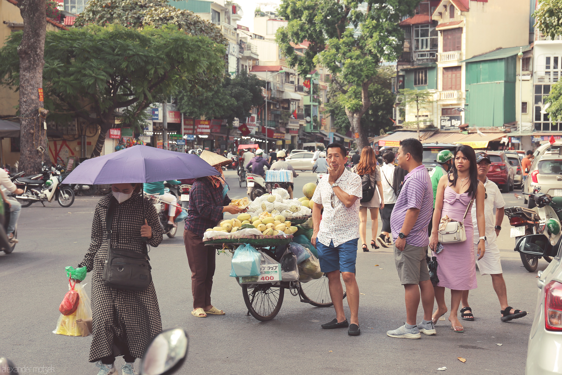 Foto von Daily life unfolds on Dong Xuan’s bustling corner, street vendors, fruits, and city dwellers glowing under Hanoi’s urban tapestry.