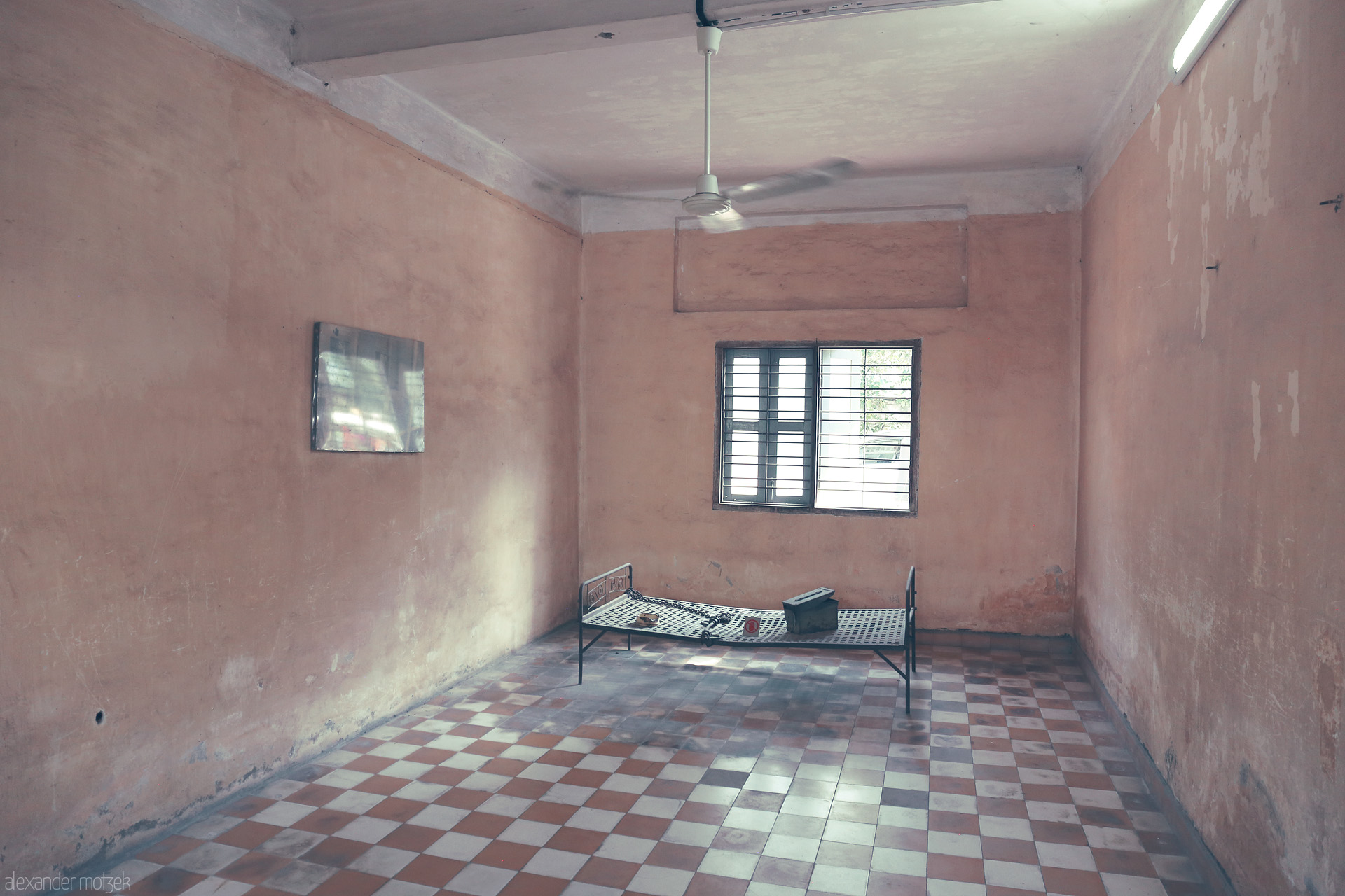 Foto von Empty cell in Tuol Sleng Genocide Museum, Phnom Penh. Stark bed, barred window, and muted walls bear witness to Cambodia's haunting history.