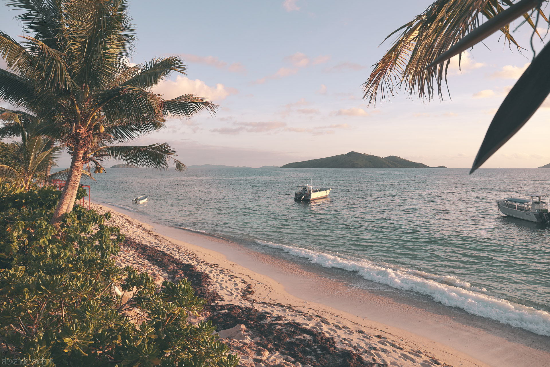 Foto von Palm-fringed beach at sunset, soft surf and anchored boats looking toward distant islands in Tokoriki, Fiji.
