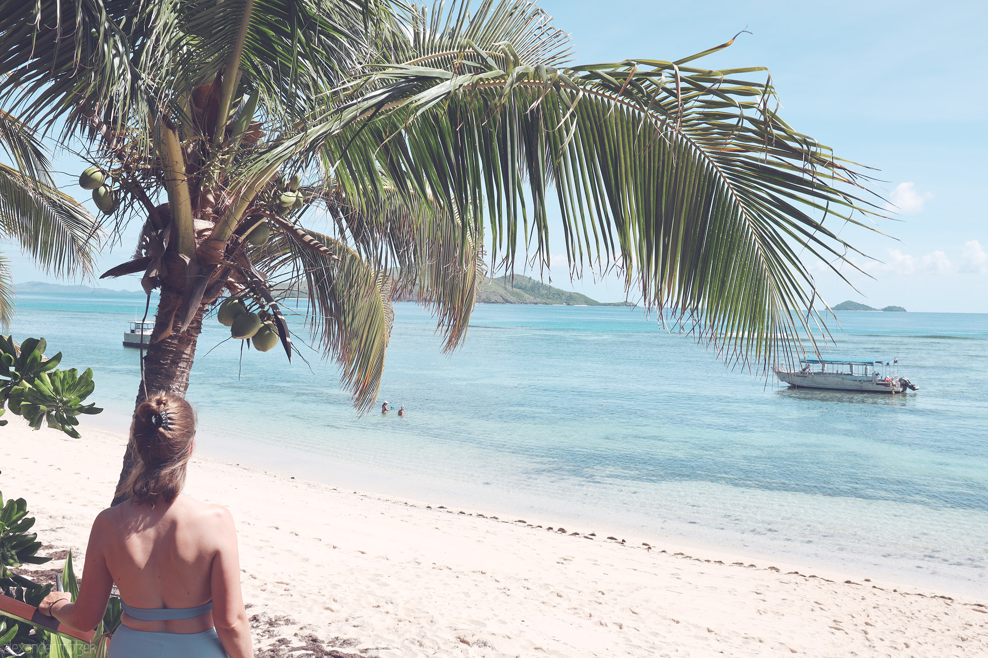 Foto von Under a coconut palm, a traveler watches boats drift on Tokoriki's turquoise lagoon, Fiji—white sand and distant isles.