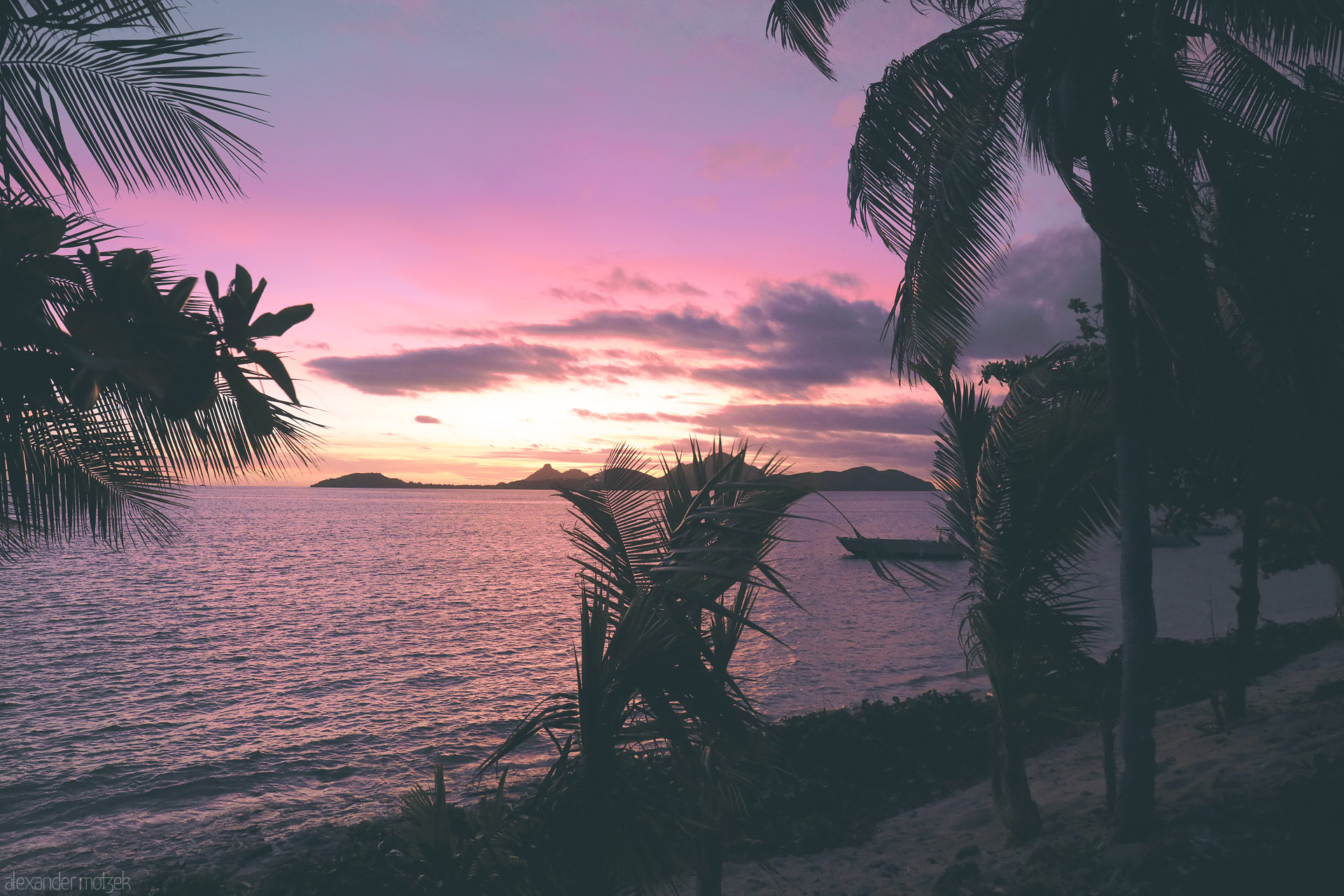 Foto von Violet sunset over the sea, palm silhouettes framing distant isles and a small boat offshore in Tokoriki, Fiji.