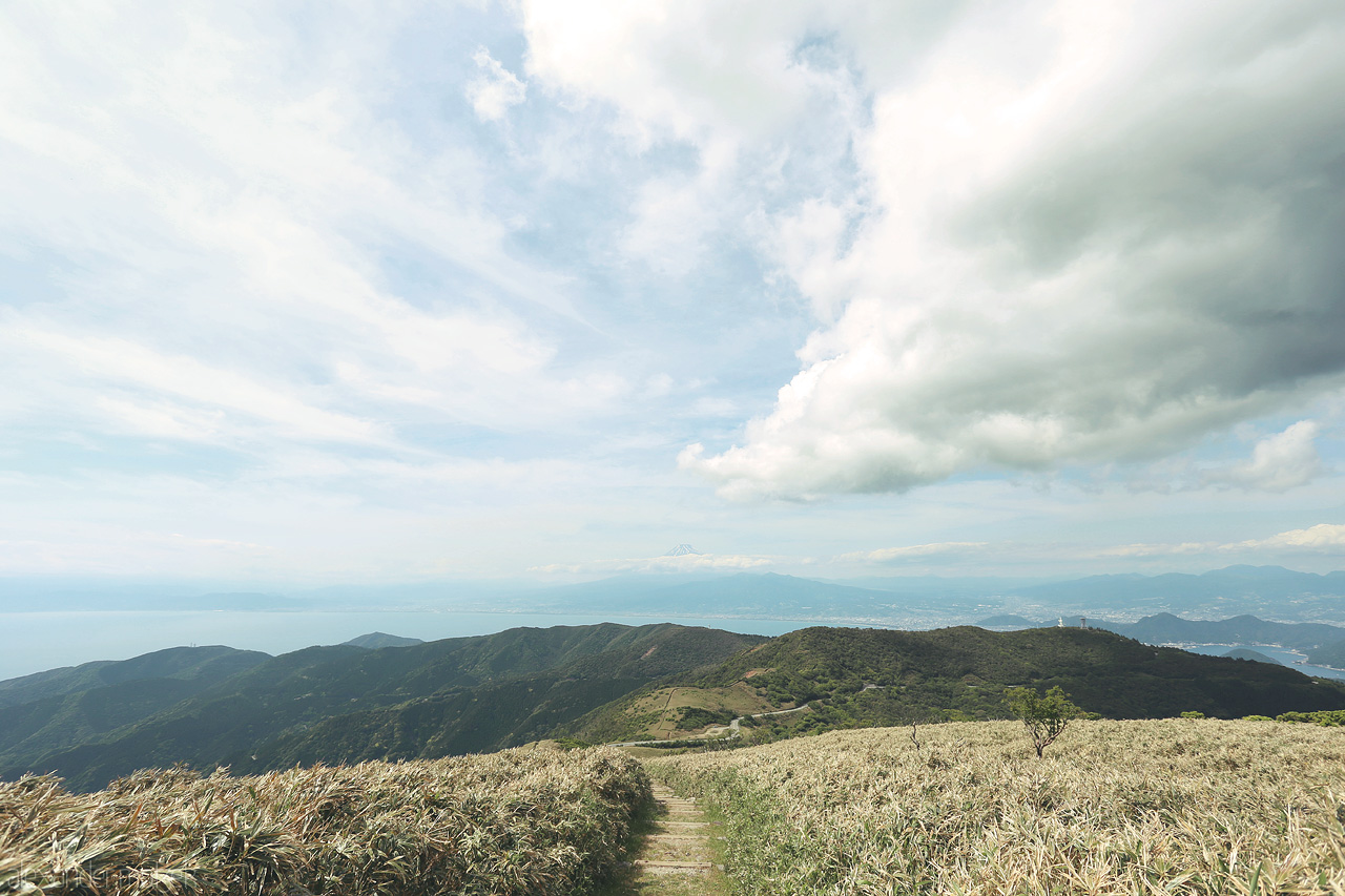 Foto von Gaze over Izu’s lush trails with Mount Fuji on the horizon under a vast, cloudy sky in Shizuoka, Japan.