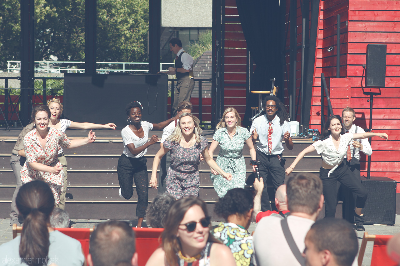 Foto von A vibrant swing dance performance graces the open-air stage by the Thames in London, showcasing joyful dancers in vintage attire.