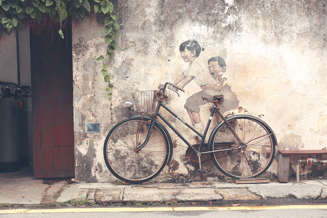 Foto von A nostalgic mural in Penang captures children on a bicycle, embodying the city's vibrant art scene and heritage charm.