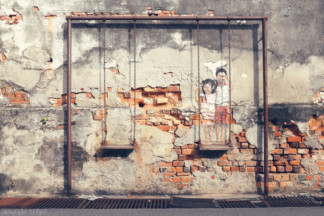 Foto von A nostalgic mural with swings on a weathered wall in Penang captures the essence of childhood and heritage.