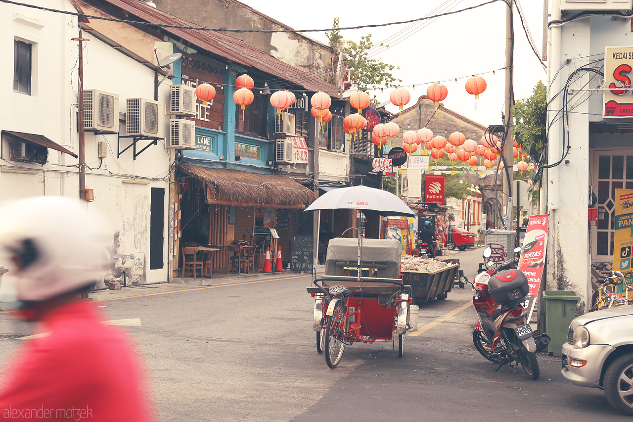 Foto von A street in Penang, Malaysia, adorned with vibrant lanterns and a classic trishaw, showcasing local culture and charm.