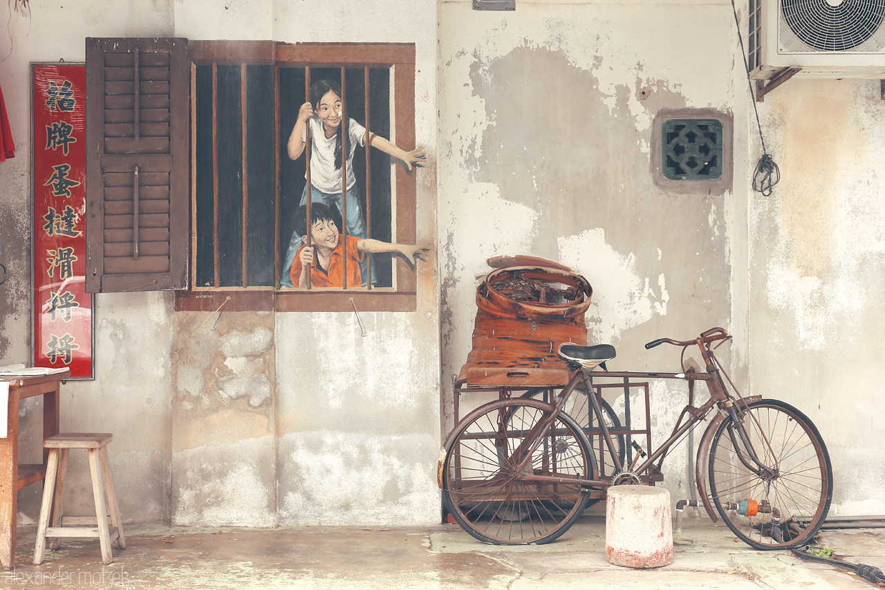 Foto von A whimsical street mural in Penang depicts children at play beside an old bicycle, capturing the spirit of Georgetown's vibrant cultural art scene.