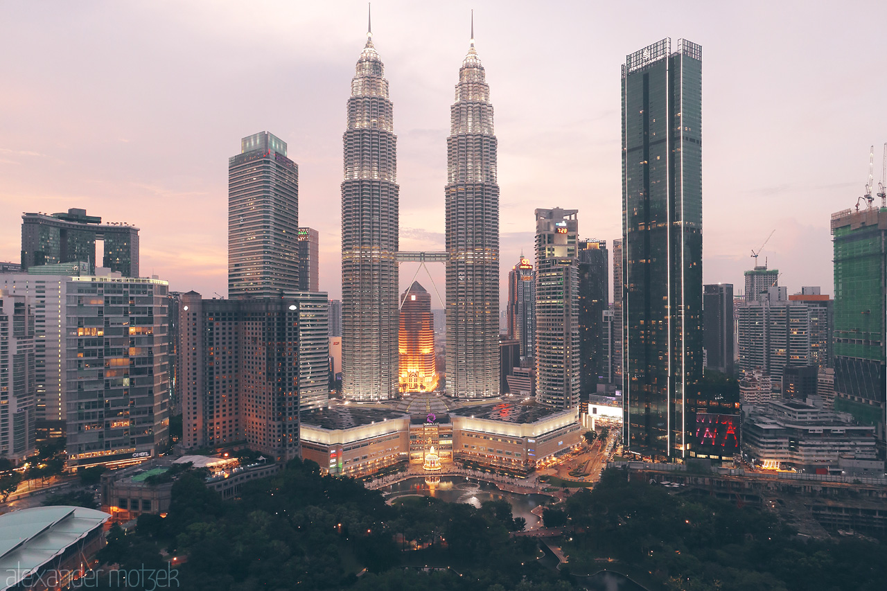 Foto von Kuala Lumpur's iconic skyline with the Petronas Towers glowing at dusk, amidst a backdrop of urban architecture and a serene evening sky.