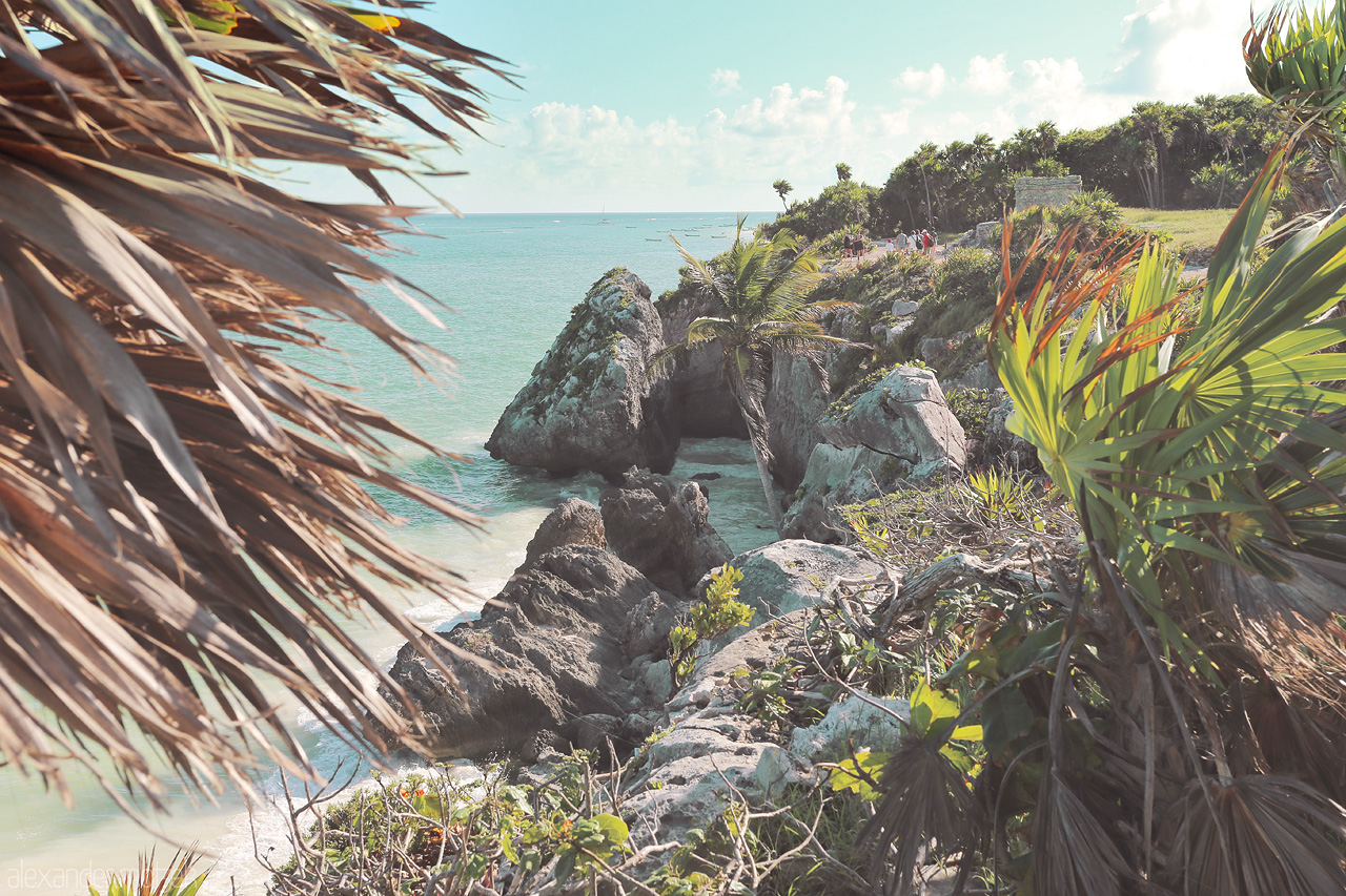 Foto von Lush greenery and rocky cliffs frame the serene turquoise waters of Tulum's coastline.