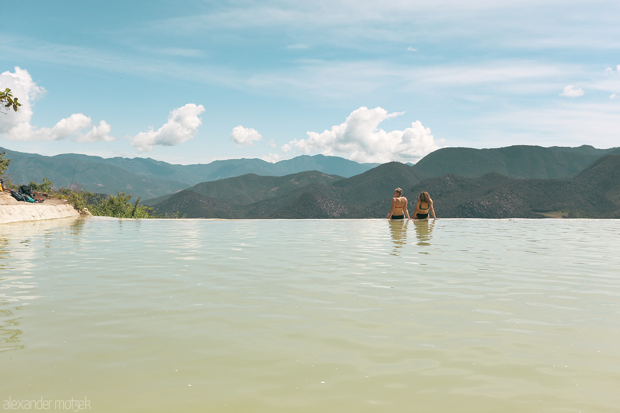 Foto von Two visitors wade in tranquil waters against a backdrop of Oaxaca's rolling hills.
