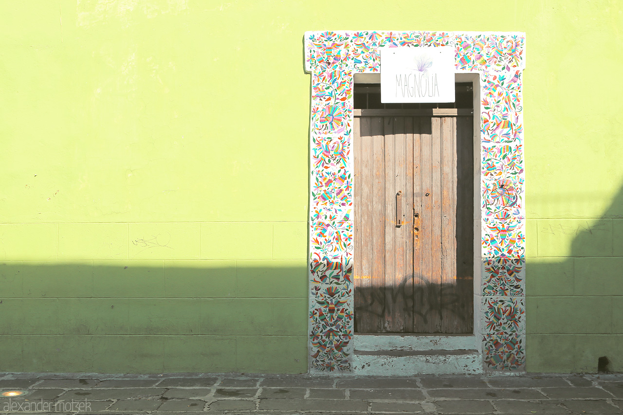 Foto von Vibrant tiled archway & rustic door on a sunbathed lime wall capture the essence of Puebla, Mexico.