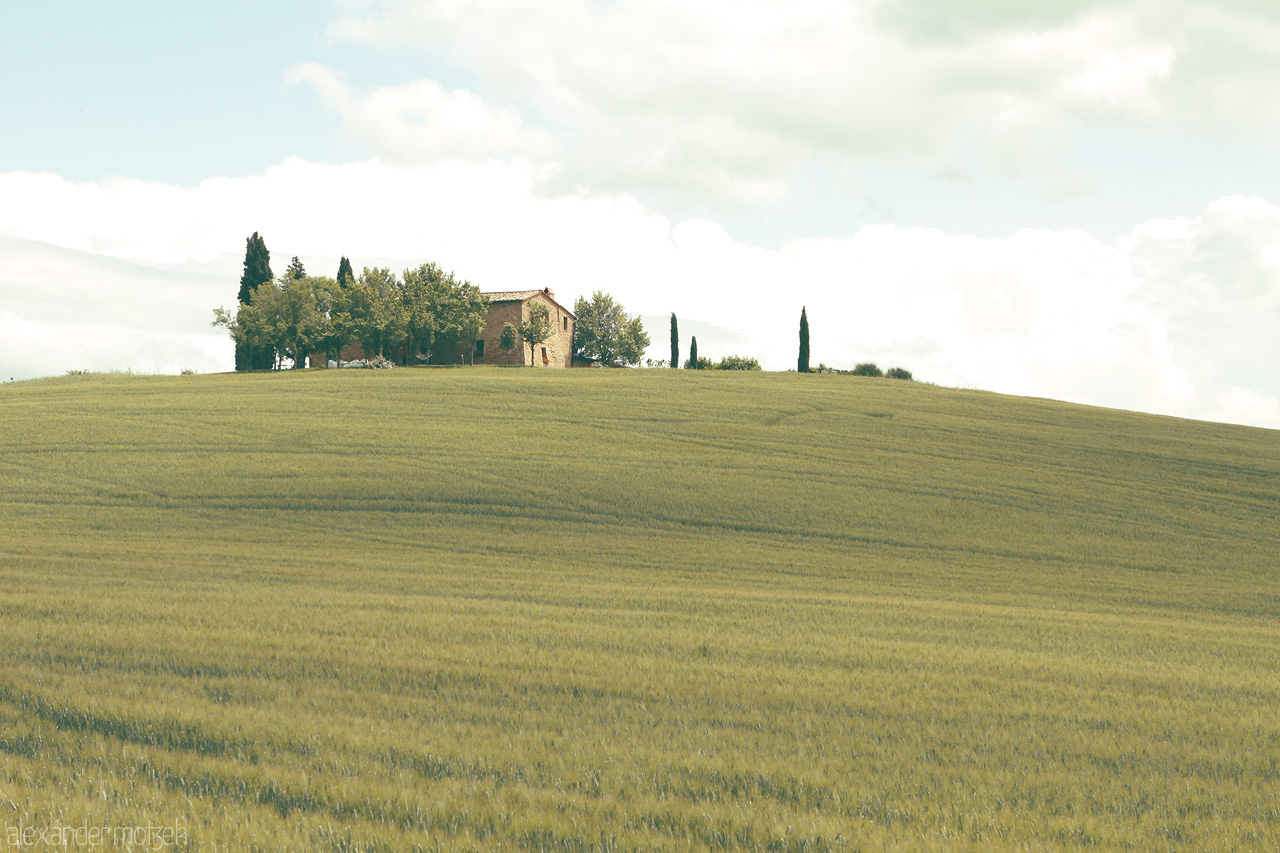 Serenity in Toscana Foto von Rolling Tuscan hills embrace a solitary farmhouse under a sky of gentle clouds.